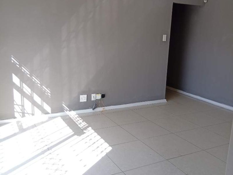 A bright, empty living room featuring neutral grey walls and light-colored floor tiles, offering a clean and versatile space for potential residents.