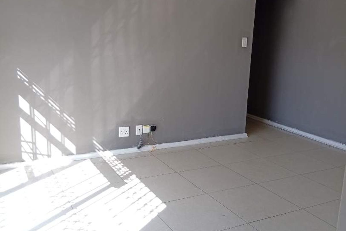 A bright, empty living room featuring neutral grey walls and light-colored floor tiles, offering a clean and versatile space for potential residents.