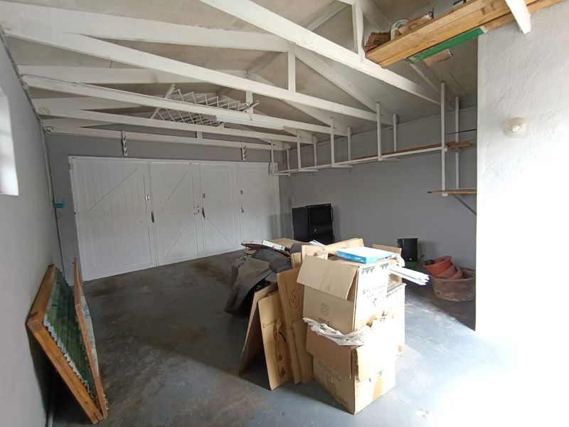 A functional garage space featuring exposed roof trusses, built-in wall shelving, and double garage doors with concrete flooring.