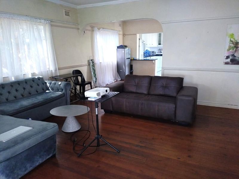 Open plan living area featuring hardwood flooring and an arched transition to the kitchen, providing a functional layout with potential for cosmetic updates.