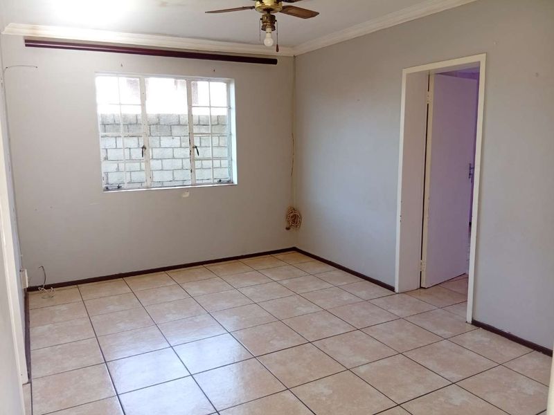 An empty living room featuring tiled flooring, a ceiling fan, and a window with security bars, ready for personalization.
