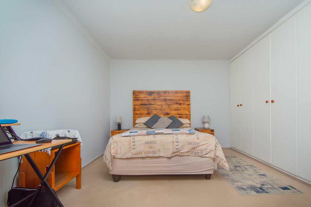 A well-proportioned bedroom featuring neutral wall finishes, carpeted flooring, and extensive built-in cupboard storage.