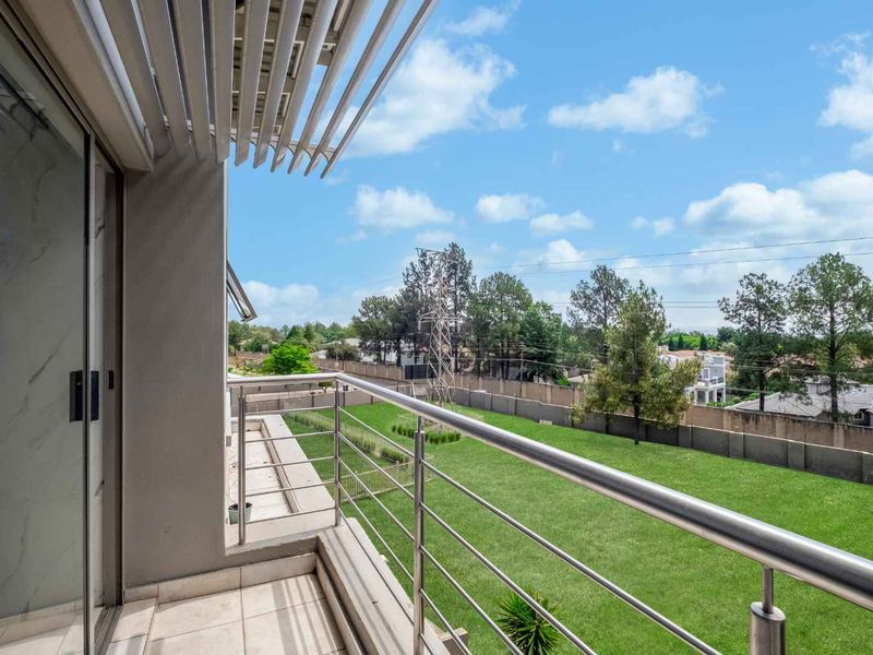 A modern balcony featuring a stainless steel balustrade, tiled flooring, and a louvred roof, offering an open view of the surrounding garden and neighborhood.