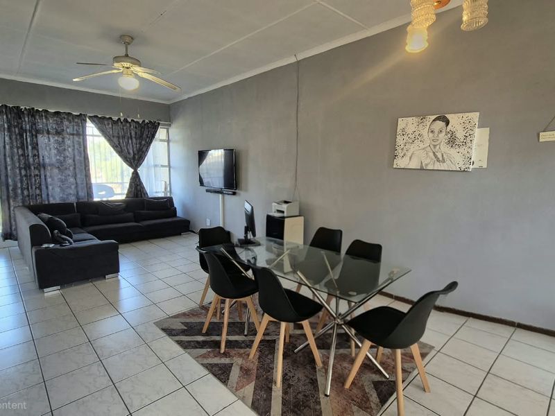 Spacious open-plan living and dining area featuring neutral tiled flooring, a ceiling fan, and large sliding glass doors providing natural light.