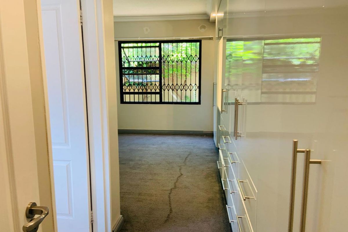 A bedroom featuring extensive built-in high-gloss cabinetry and a window fitted with security bars.