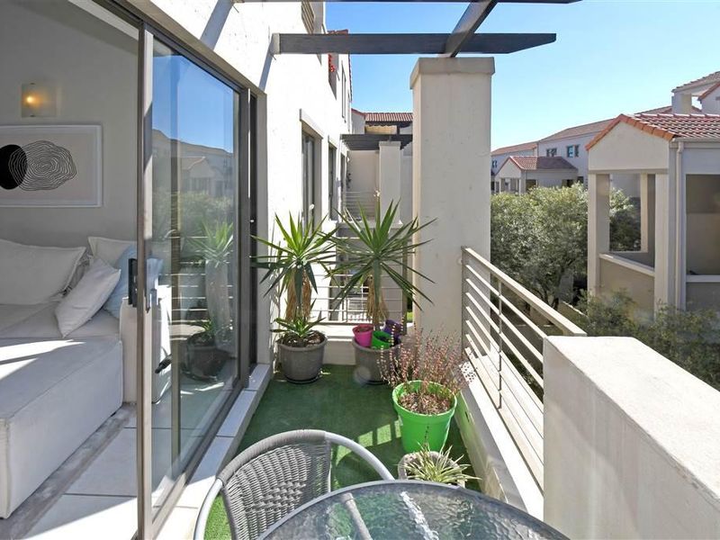 A well-maintained balcony featuring a pergola, metal balustrade, and sliding glass door access to the interior living space.