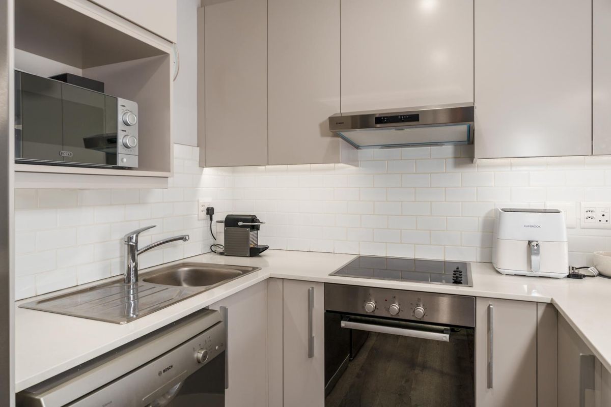 Modern kitchen featuring sleek cabinetry, stone countertops, subway tile backsplash, and integrated stainless steel appliances including an oven, hob, and extractor fan.