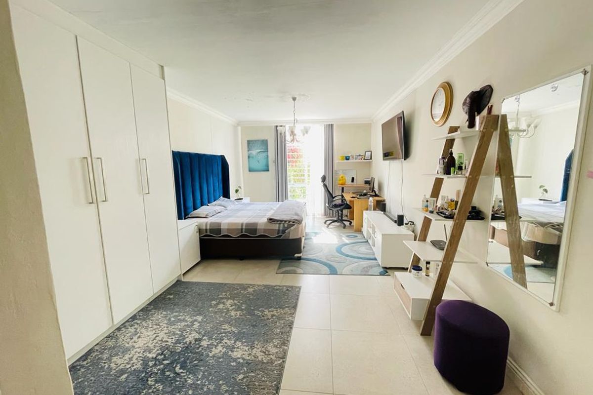 Spacious bedroom featuring large built-in wardrobes, tiled flooring, and access to a balcony through a sliding door.