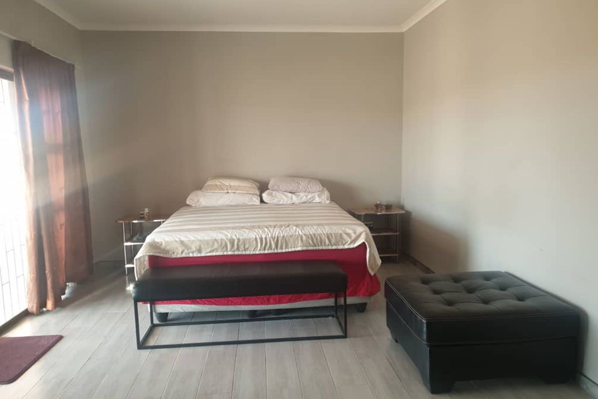 A spacious bedroom featuring light-toned tiled flooring, neutral wall finishes, and a sliding door providing access to the exterior.