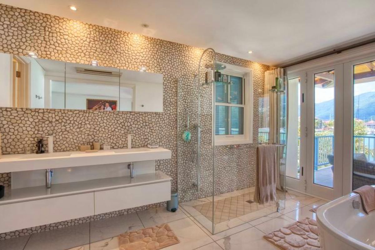 Modern bathroom featuring a double vanity, glass-enclosed shower, freestanding bathtub, and pebble-tiled feature walls with direct access to a private balcony.