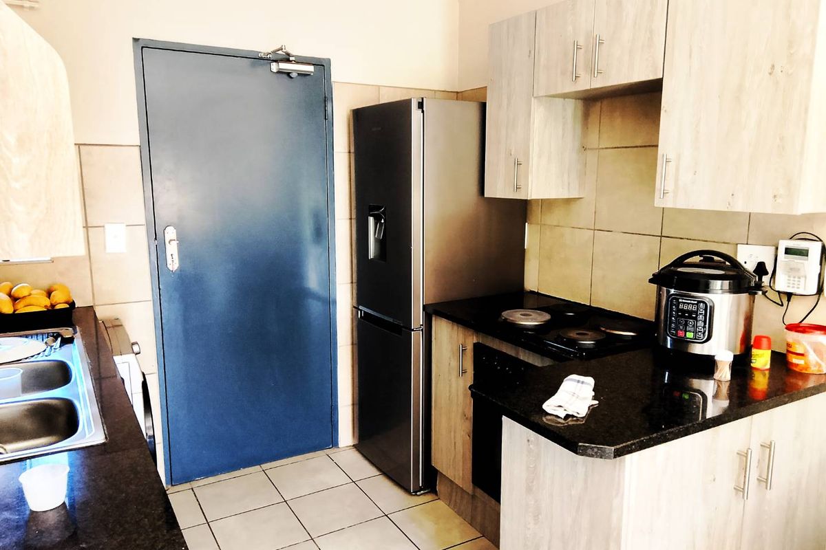 Compact kitchen featuring light wood-look cabinetry, dark granite countertops, a built-in electric hob, and tiled flooring.