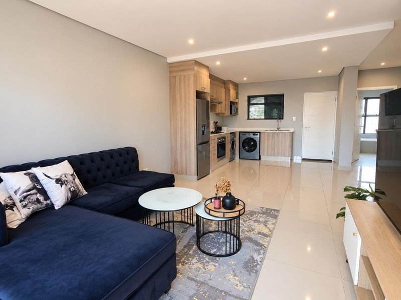 Modern open-plan living area featuring a sleek kitchen with built-in appliances, high-gloss floor tiles, and recessed lighting throughout the space.