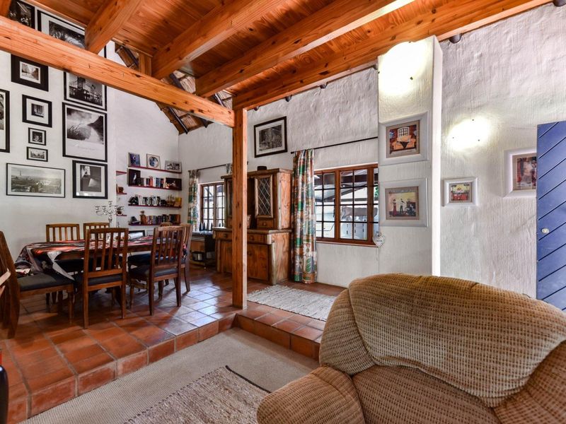 Open-plan living and dining area featuring rustic exposed timber beams, terracotta flooring, and a raised dining platform with built-in shelving.