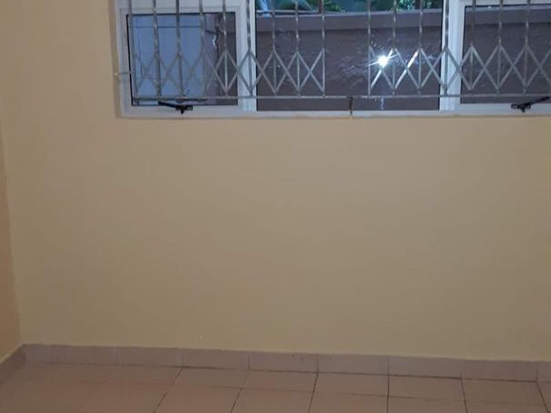 An empty bedroom featuring tiled flooring and a window fitted with security bars.
