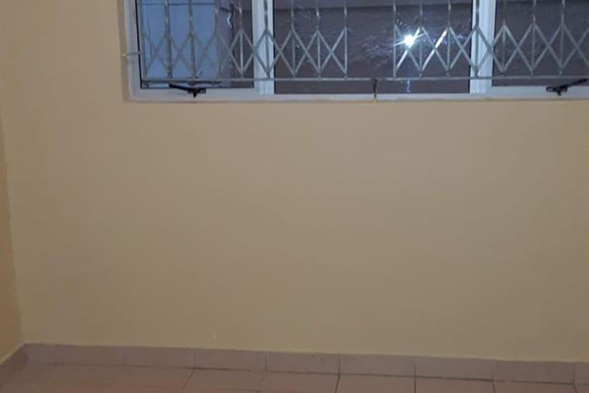 An empty bedroom featuring tiled flooring and a window fitted with security bars.