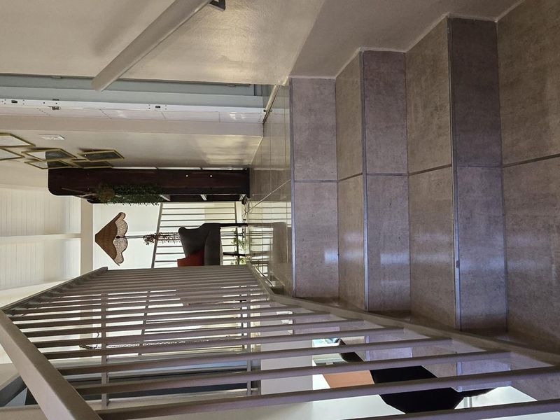 A bright hallway featuring a tiled staircase with a metal balustrade and an exposed beam ceiling, providing a clean and modern transition between levels.
