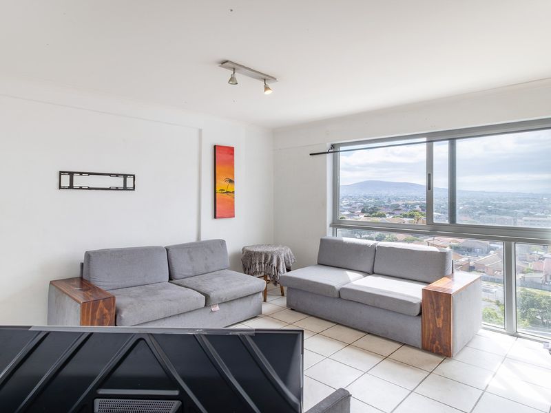 A bright living room featuring large sliding windows with expansive city views, tiled flooring, and neutral wall finishes.