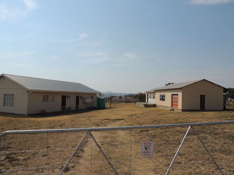 A view of the rear yard featuring two separate structures, a water tank, and a wire mesh perimeter fence.