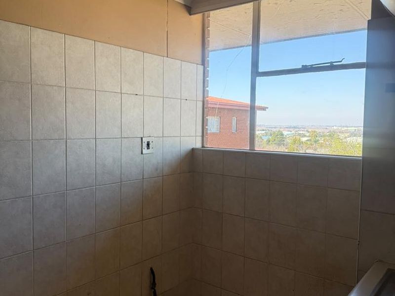 A compact kitchen area featuring tiled walls, a stainless steel sink, and a window with a view, currently in need of cosmetic updates.