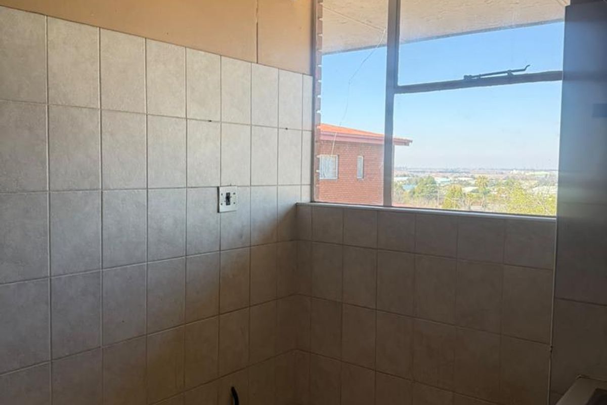 A compact kitchen area featuring tiled walls, a stainless steel sink, and a window with a view, currently in need of cosmetic updates.