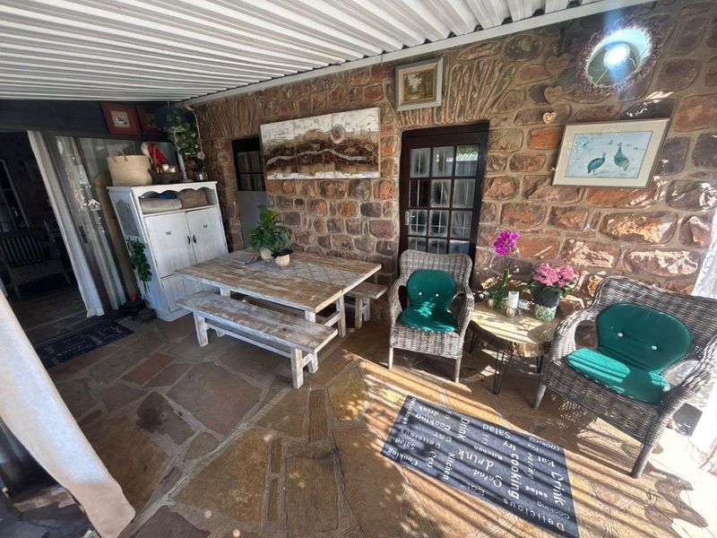 A covered patio area featuring rustic stone wall cladding, durable flagstone flooring, and a corrugated roof, providing a charming outdoor entertainment space.