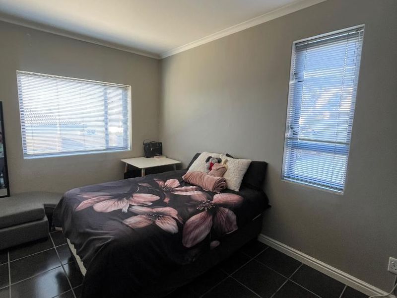 A bedroom featuring dark tiled flooring, neutral wall paint, and dual windows fitted with venetian blinds.