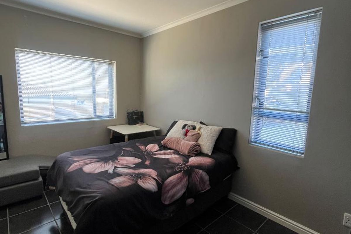 A bedroom featuring dark tiled flooring, neutral wall paint, and dual windows fitted with venetian blinds.