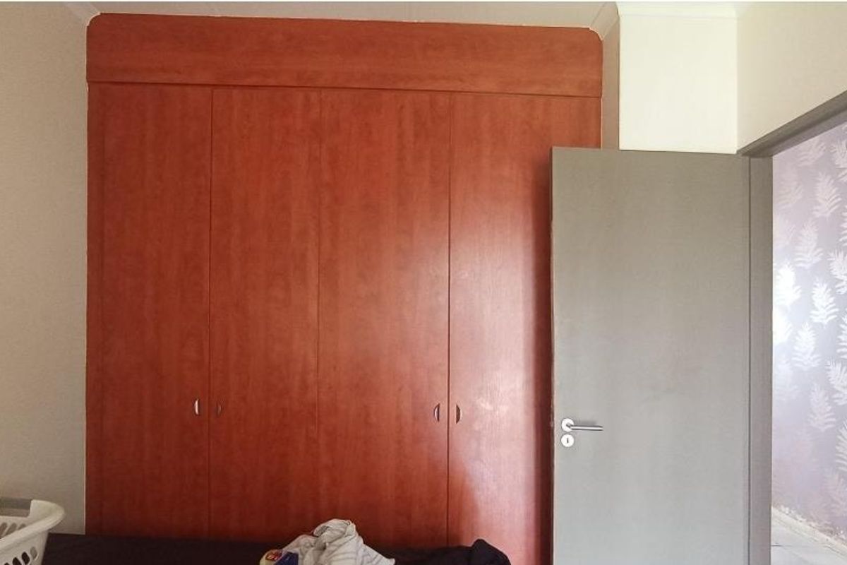 A bedroom featuring built-in wooden cupboards and a doorway leading to an adjacent space with patterned wallpaper.