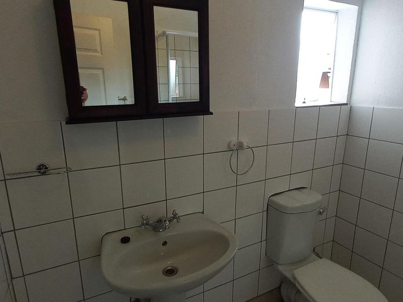 A functional bathroom featuring a pedestal washbasin, toilet, and wall-mounted medicine cabinet, finished with white ceramic wall tiles.