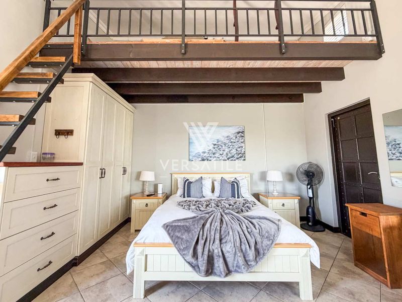 A bedroom featuring a mezzanine level with a timber staircase, exposed ceiling beams, built-in cabinetry, and tiled flooring.