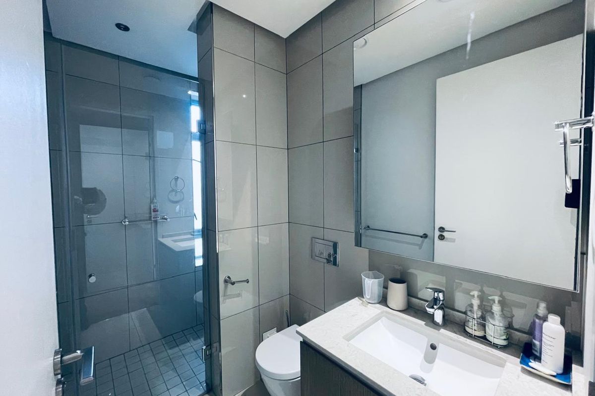 Modern bathroom featuring a glass-enclosed shower, wall-mounted toilet, and a sleek vanity with an integrated sink and large mirror.
