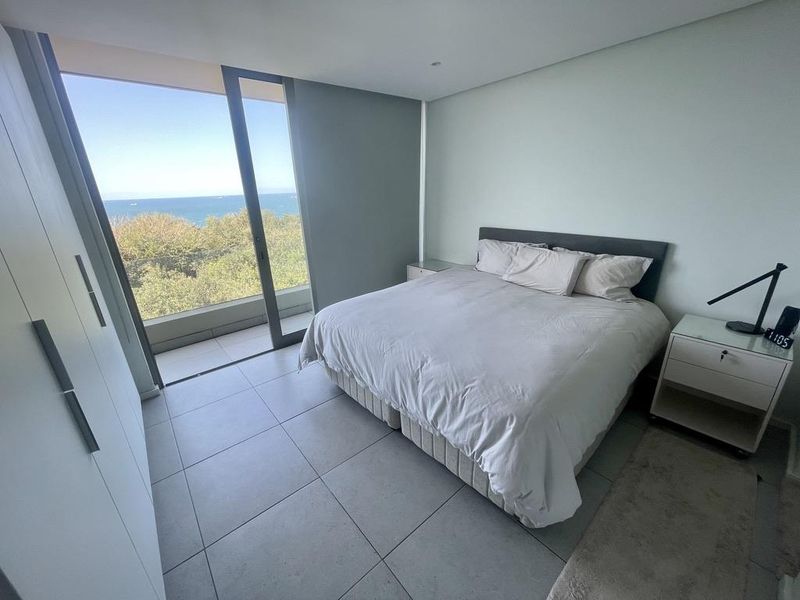 Modern bedroom featuring large floor-to-ceiling sliding glass doors that open to a balcony with scenic ocean views and built-in cabinetry.