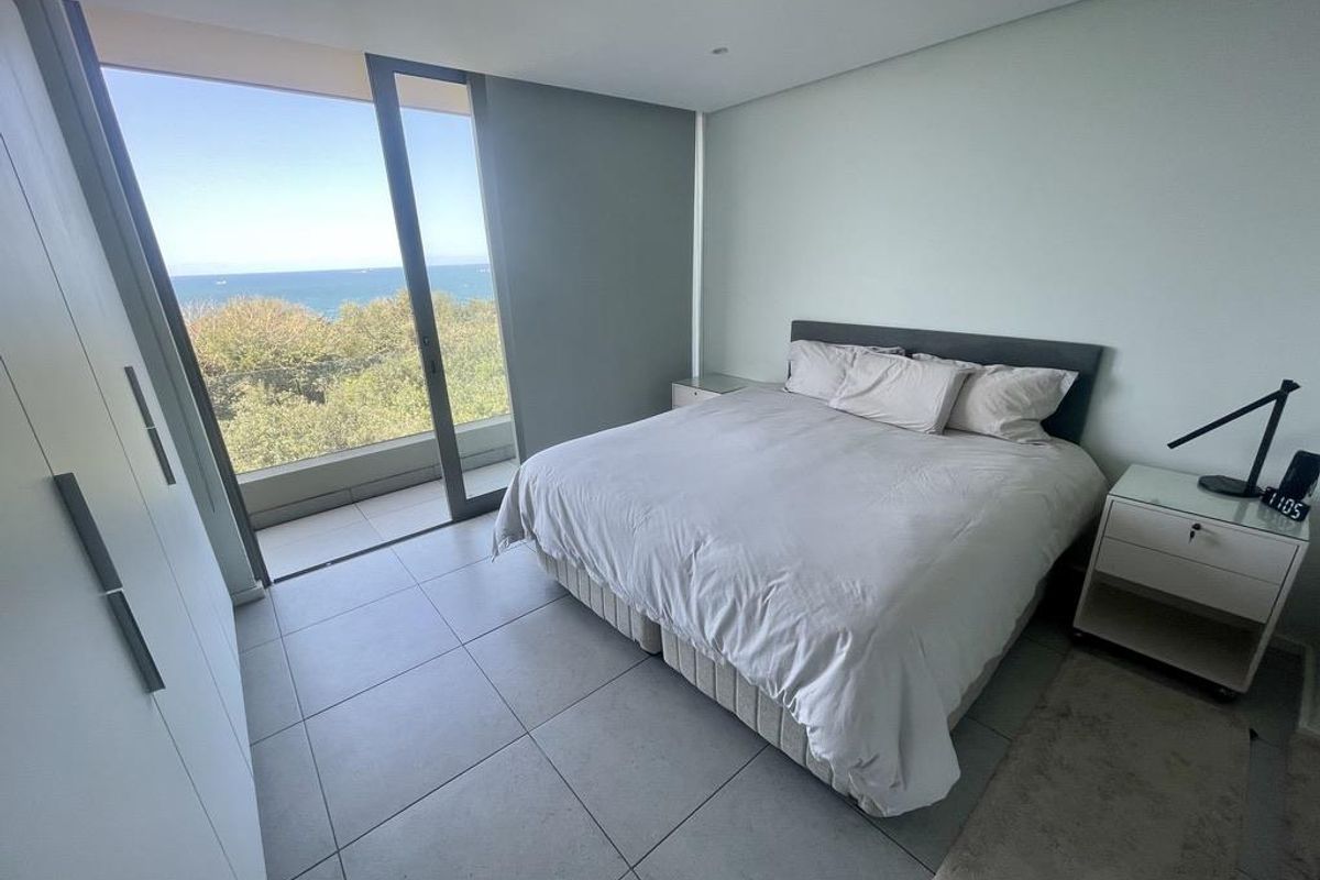 Modern bedroom featuring large floor-to-ceiling sliding glass doors that open to a balcony with scenic ocean views and built-in cabinetry.