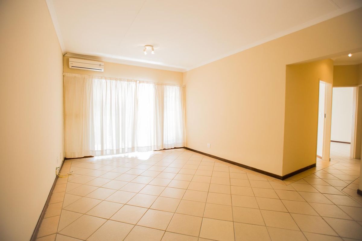 A spacious, empty living area featuring neutral ceramic floor tiles, coved cornicing, and a wall-mounted split-system air conditioning unit.