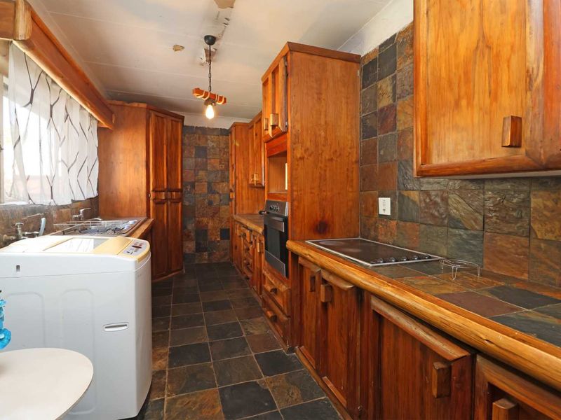 A dated kitchen featuring extensive wooden cabinetry, slate tile surfaces, and integrated appliances, requiring cosmetic updates to modernize the space.