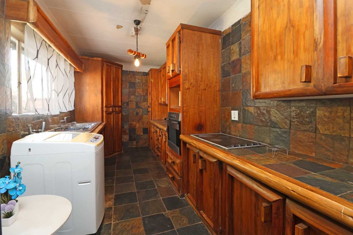 A dated kitchen featuring extensive wooden cabinetry, slate tile surfaces, and integrated appliances, requiring cosmetic updates to modernize the space.