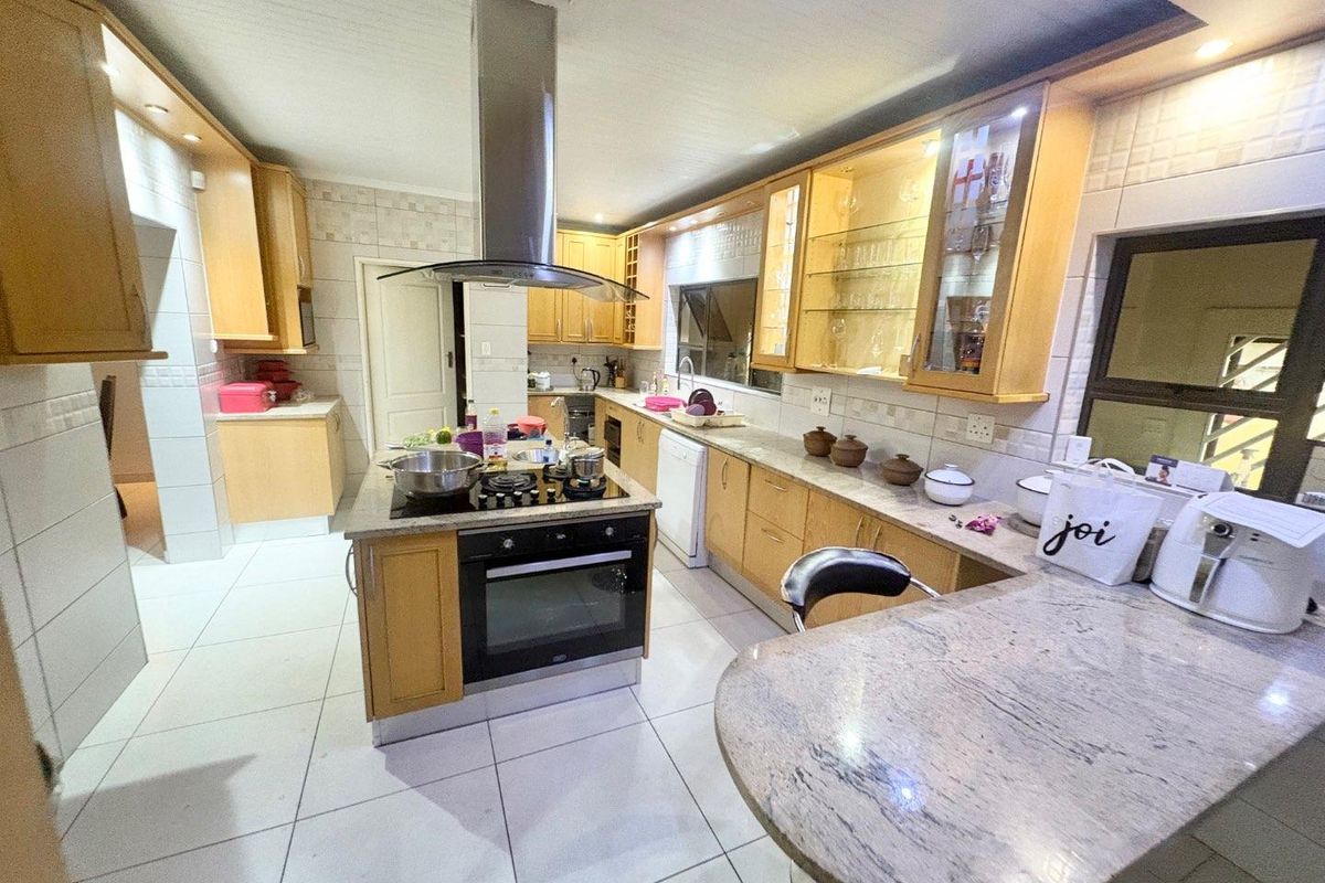 Spacious kitchen featuring light wood cabinetry, granite countertops, a central island with a built-in oven and hob, and a breakfast bar area.