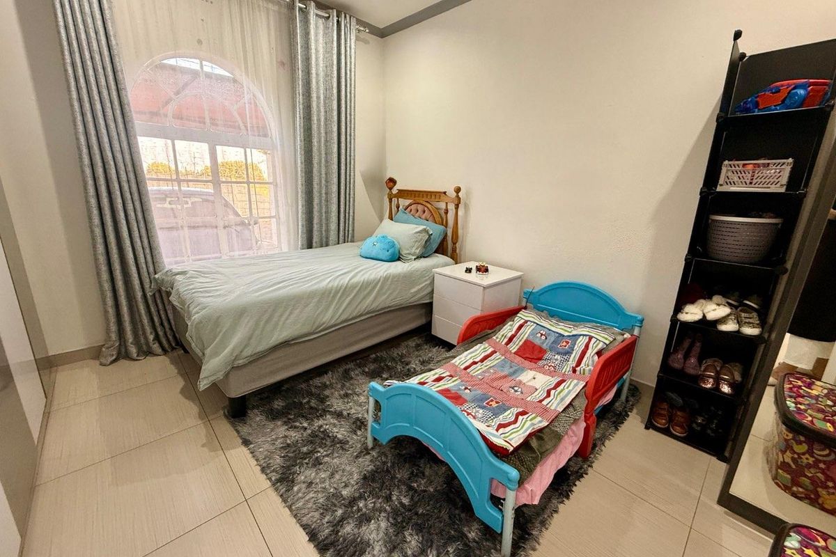 A well-maintained bedroom featuring large arched windows, tiled flooring, and neutral wall finishes, providing a bright and functional living space.