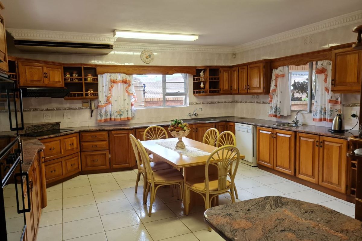 Spacious kitchen featuring extensive wooden cabinetry, granite countertops, double sinks, and a central dining area with tiled flooring.