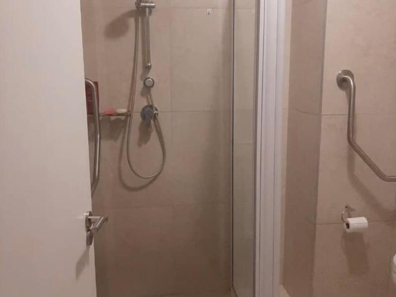 A functional bathroom featuring a tiled shower enclosure with a glass door and wall-mounted grab rails for accessibility.