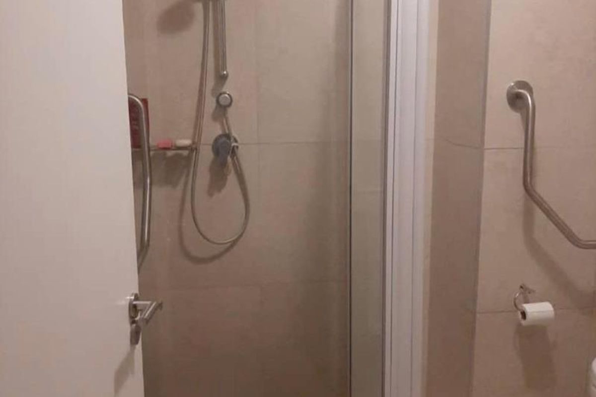 A functional bathroom featuring a tiled shower enclosure with a glass door and wall-mounted grab rails for accessibility.