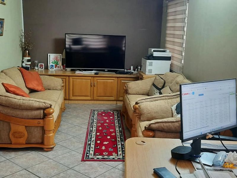 A living room featuring tiled flooring, built-in cabinetry, and roller blinds, currently utilized as a multi-purpose living and workspace area.