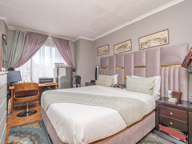 A bedroom featuring tiled flooring and coving, currently furnished with a large bed and integrated headboard.
