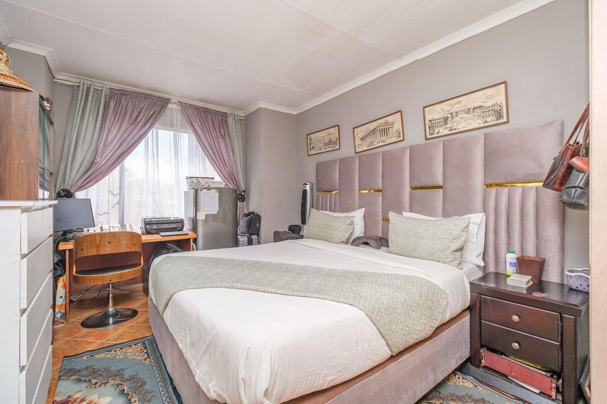 A bedroom featuring tiled flooring and coving, currently furnished with a large bed and integrated headboard.
