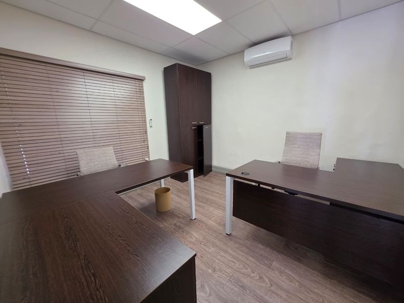 A functional office space featuring laminate flooring, a suspended ceiling, built-in storage cabinetry, and a wall-mounted split-system air conditioner.