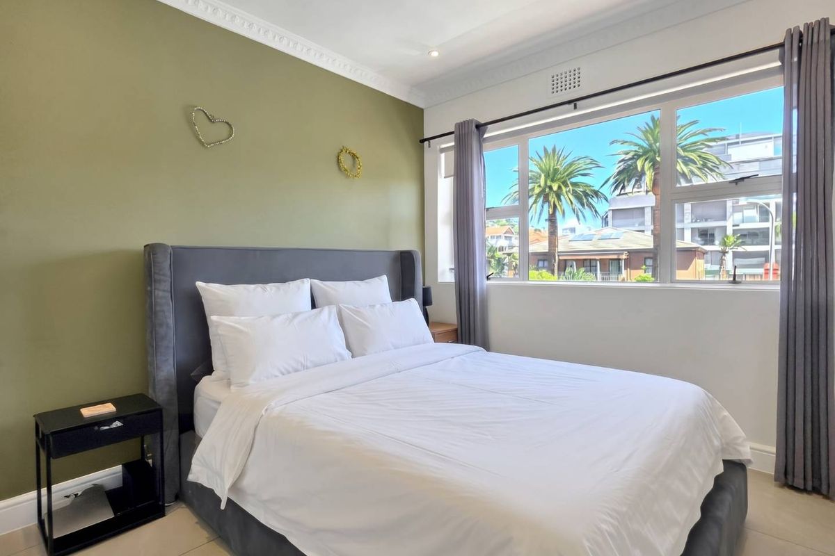 A bright and well-maintained bedroom featuring crown molding, large windows with natural light, and neutral tiled flooring.