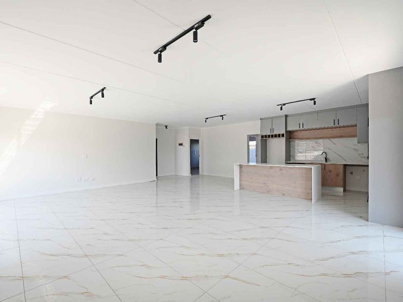 Spacious open-plan living area featuring high-gloss marble-look floor tiles, modern kitchen cabinetry with an island, and contemporary track lighting throughout.