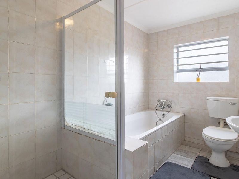 A functional bathroom featuring a built-in bathtub, separate shower enclosure, wall-mounted basin, and toilet with neutral wall tiling.