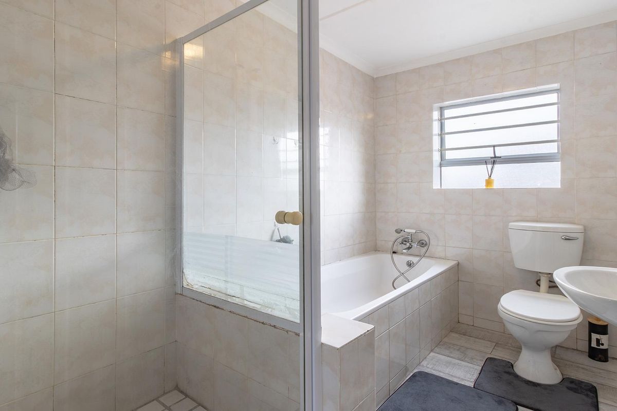 A functional bathroom featuring a built-in bathtub, separate shower enclosure, wall-mounted basin, and toilet with neutral wall tiling.