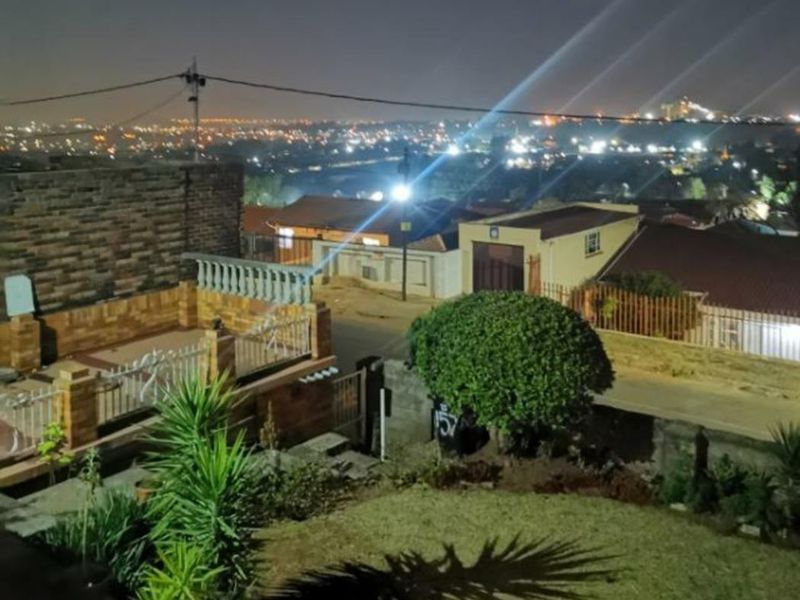 Nighttime elevated view overlooking the residential neighborhood, featuring a landscaped garden, paved patio area, and brick boundary wall.